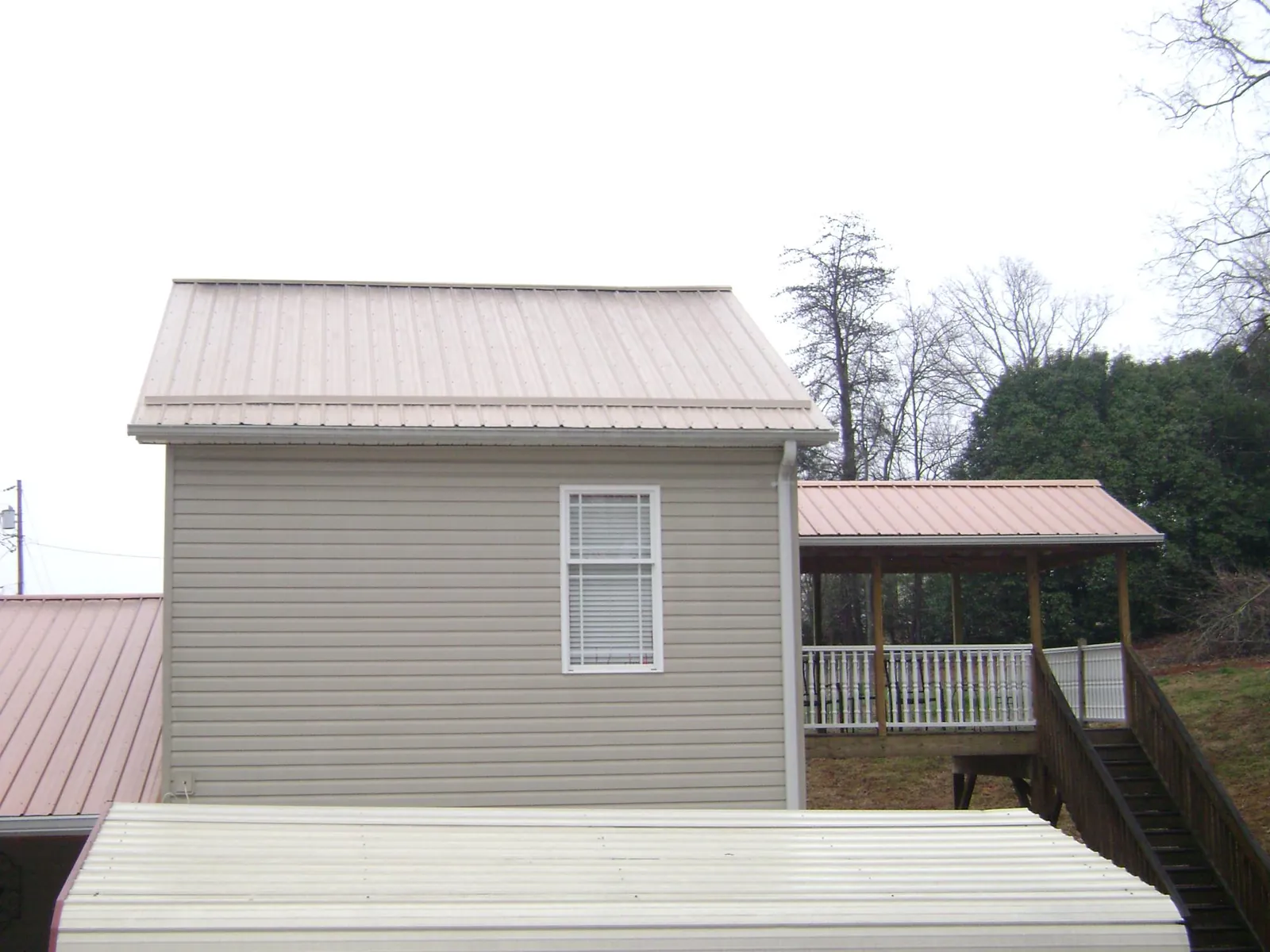 Tan metal roofs on a two story addition and attached porch, from a Roof Replacement job in Sterling